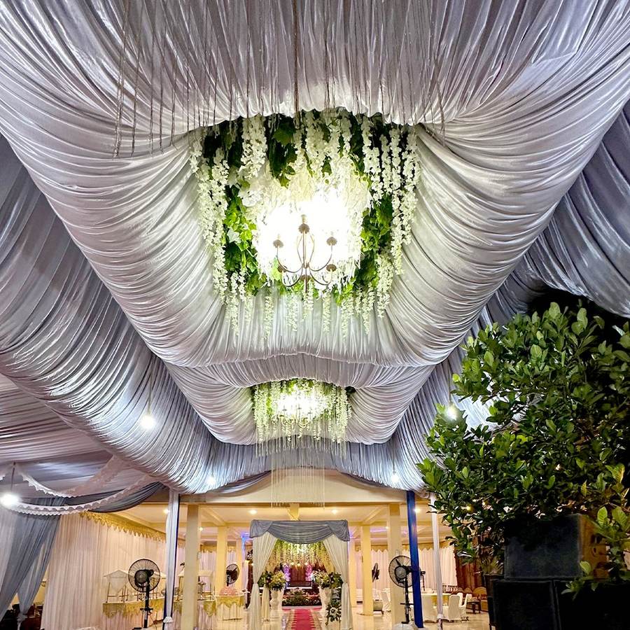 Plafon drapery putih dengan lampu gantung kristal dan untaian dedaunan