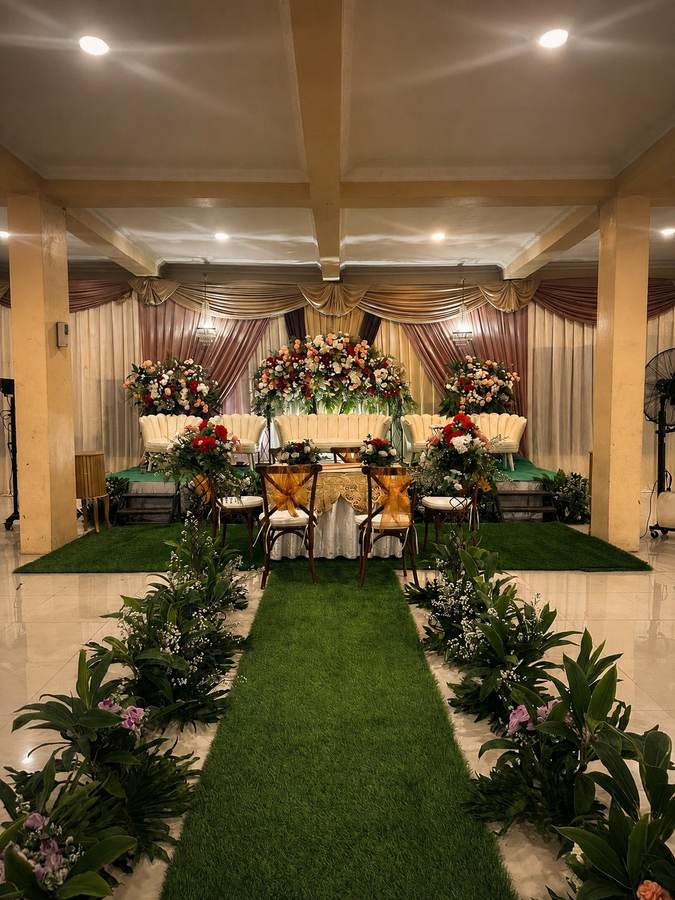 Pelaminan dengan latar drapery dan rangkaian bunga warna hangat