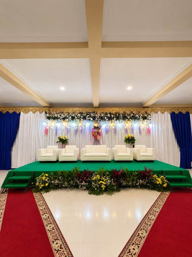 Pelaminan dengan panggung hijau, sofa krem, dan latar drapery biru
