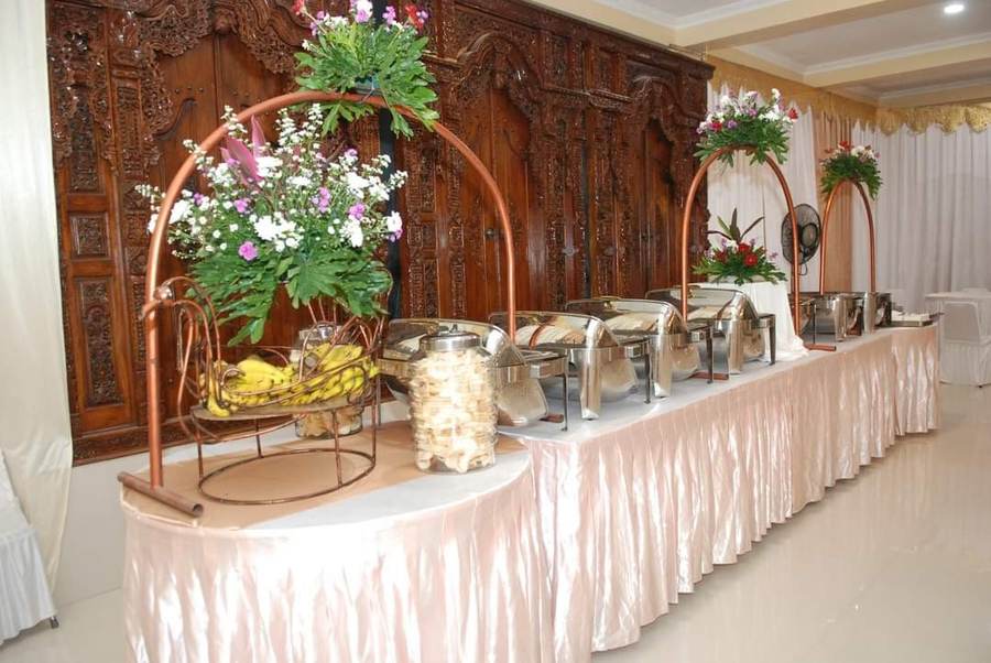 Meja prasmanan dengan chafing dish dan latar backdrop ukir kayu