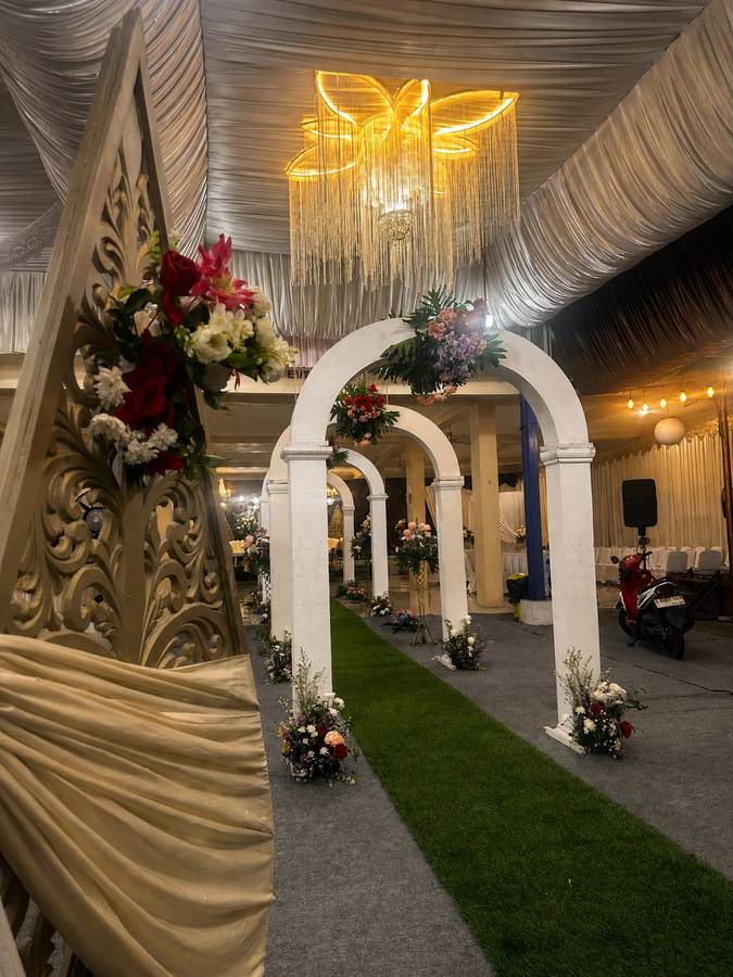 Gerbang lengkung putih dengan ornamen gunungan emas dan bunga segar