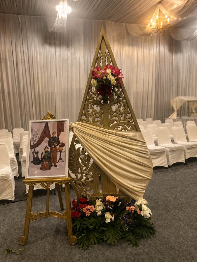 Foto pengantin berbusana adat Jawa di samping ornamen gunungan emas