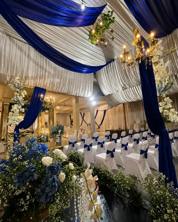 Dekorasi Navy & Gold: plafon draperi navy-putih dengan lampu kristal dan rangkaian bunga biru
